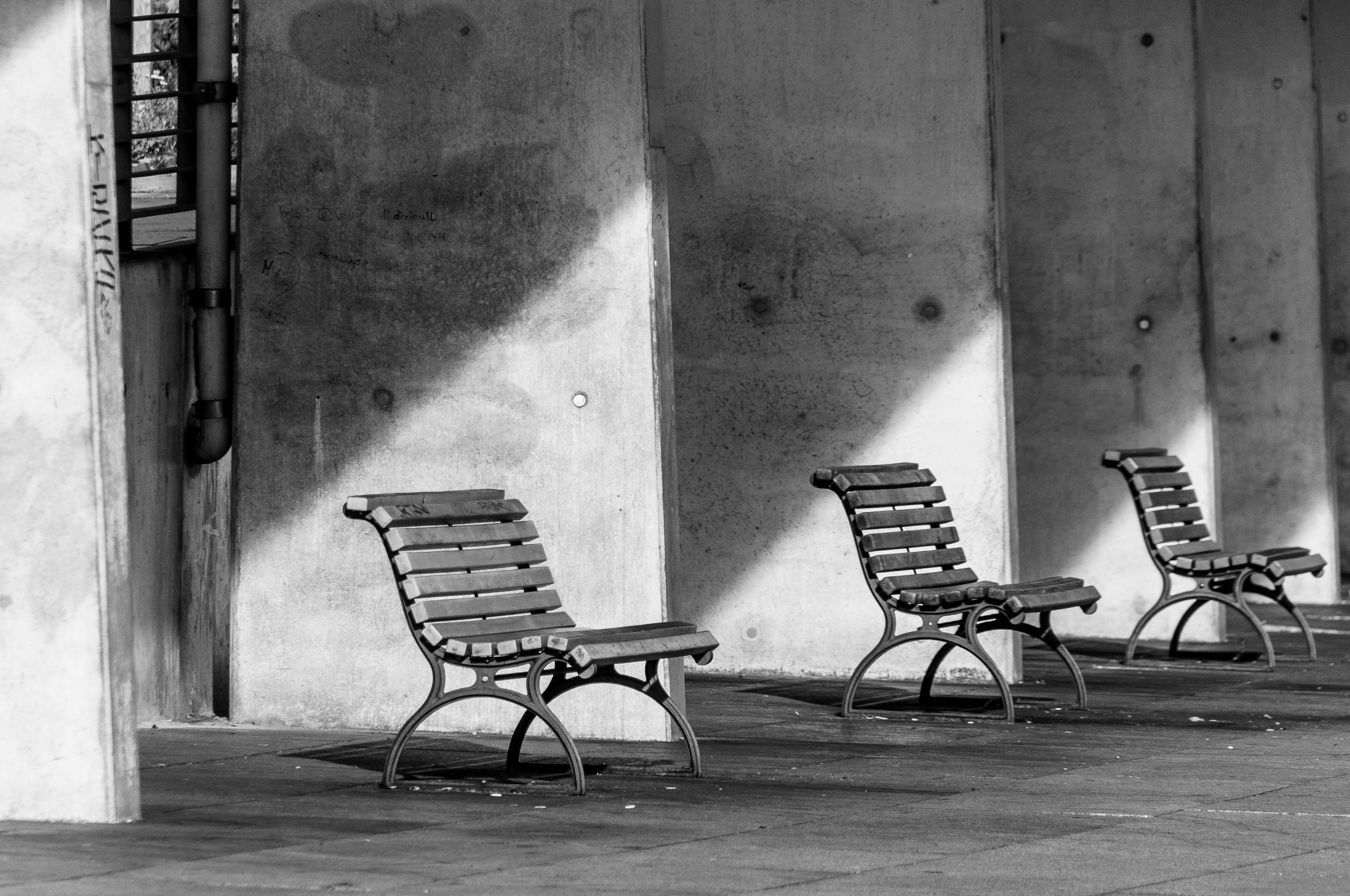 Gratis Tre panchine vuote in bianco e nero contro un muro di cemento con ombre spettacolari. Foto a disposizione