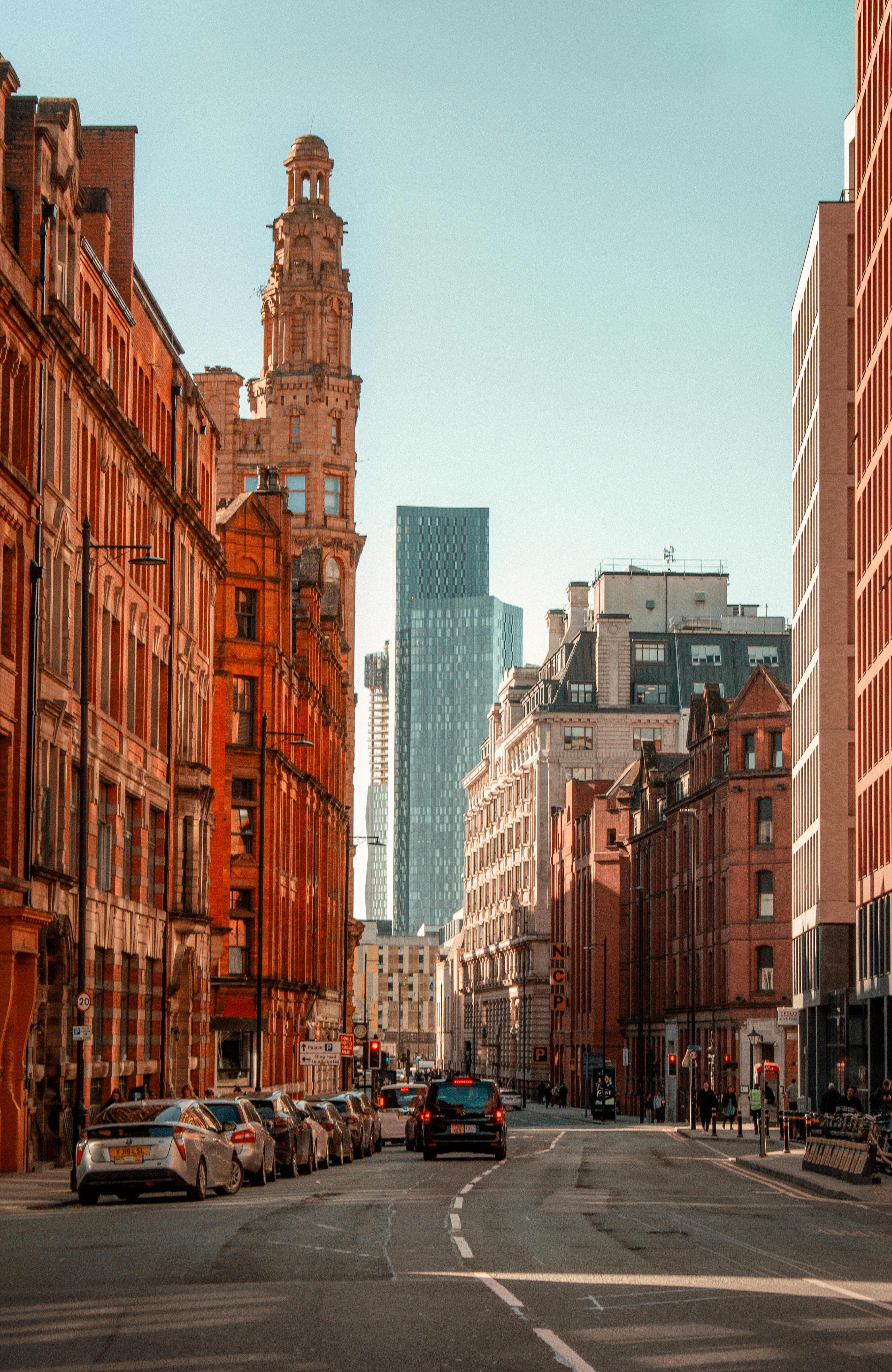 Una calle soleada de Manchester con arquitectura histórica y moderna en contraste.