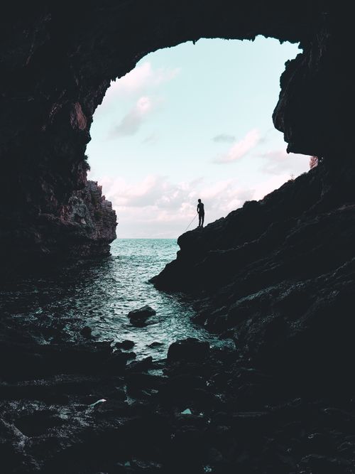 Free Dramatic silhouette of a person standing in a cave opening overlooking the ocean. Stock Photo