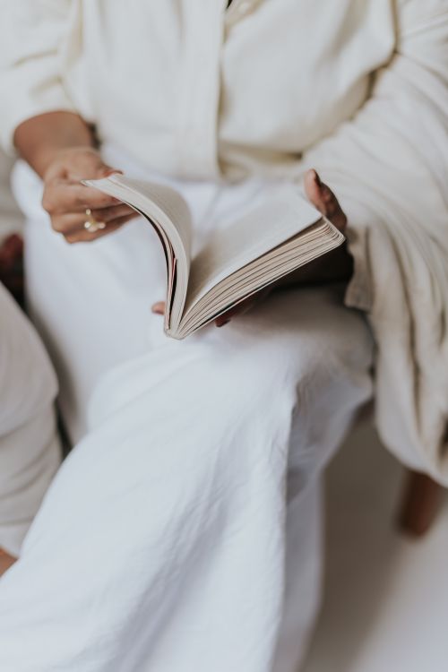 Free Close-up of a person leisurely reading a book in a cozy setting, dressed in soft white clothes. Stock Photo
