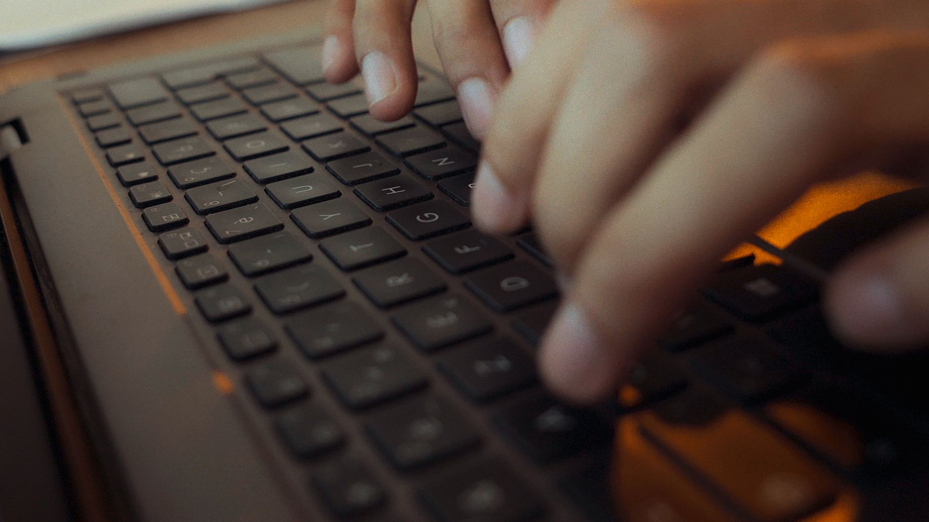 Close-up of hands typing on a laptop keyboard with moody lighting in an Algerian setting.