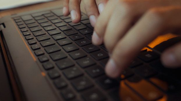 Close-up of hands typing on a laptop keyboard with moody lighting in an Algerian setting.