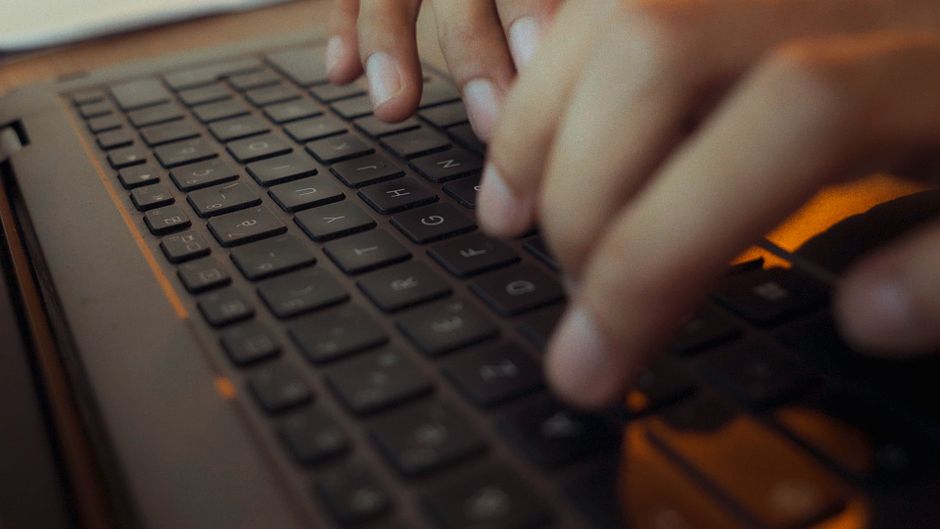 Close-up of hands typing on a laptop keyboard with moody lighting in an Algerian setting.