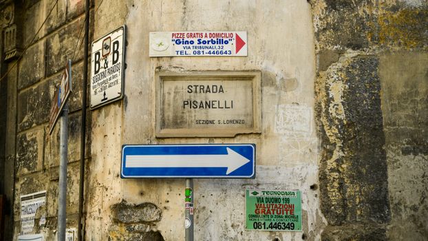 Textured street signs on a rustic building wall in Naples, Italy.