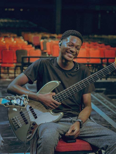 Smiling young musician holding a guitar, seated in an empty concert hall in Accra, Ghana.