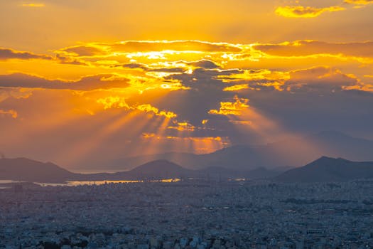 Stunning golden sunset with rays illuminating a city skyline and distant mountains.