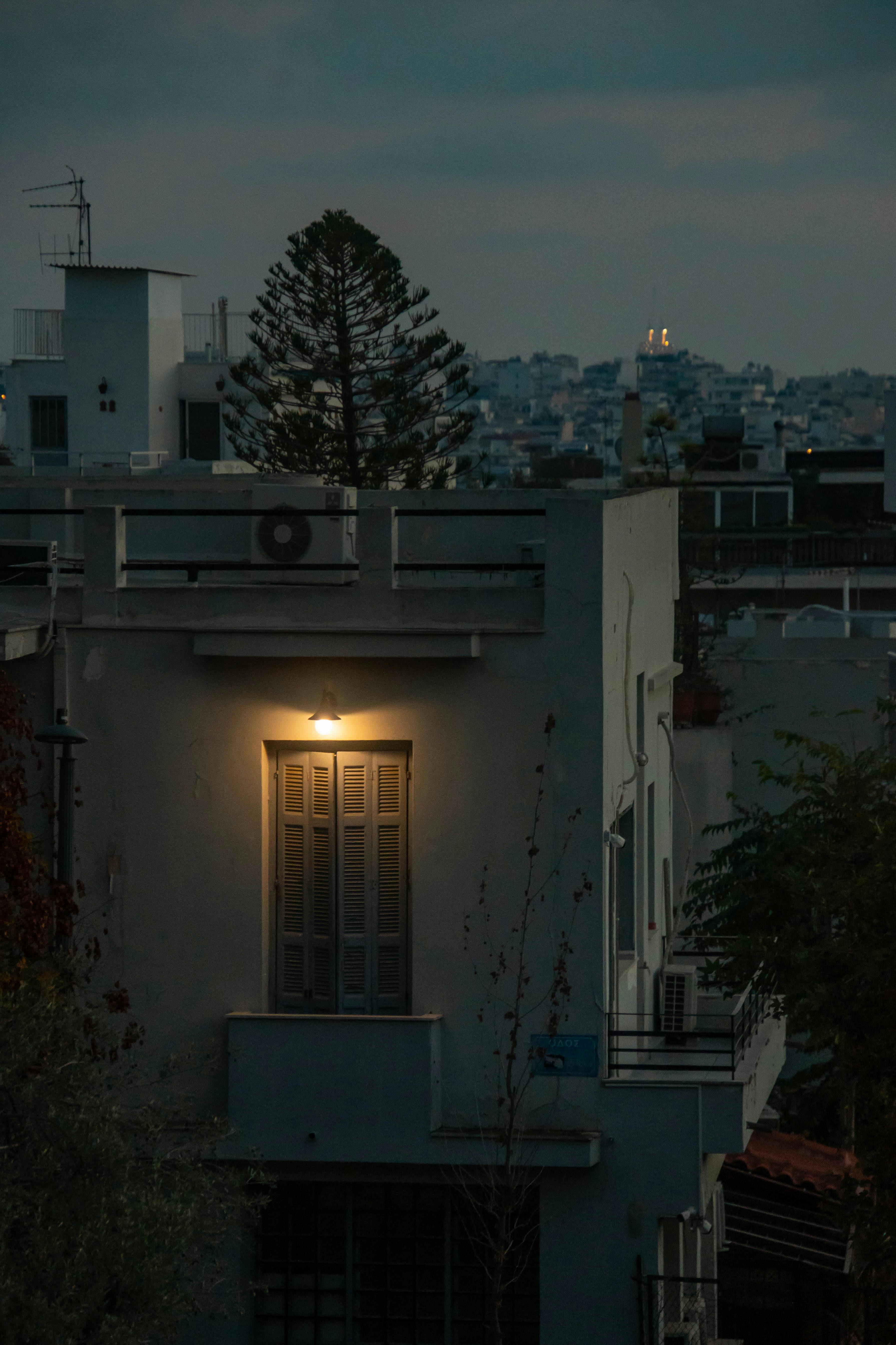 grátis Um prédio urbano com iluminação tênue ao entardecer, apresentando uma janela brilhante contra um pano de fundo da cidade. Foto profissional