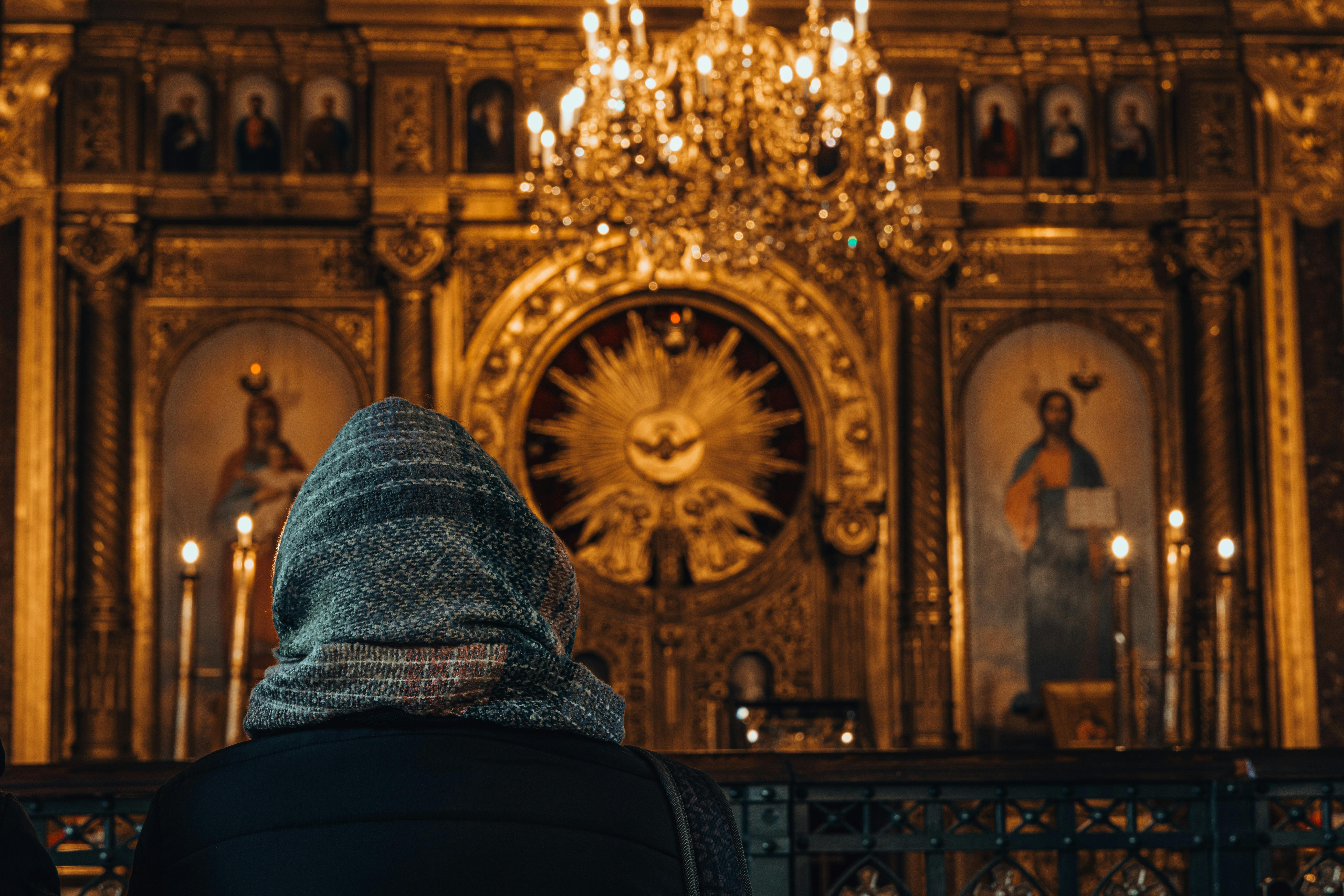 A person in a headscarf sits before an ornate church altar in İstanbul, Türkiye, with chandeliers above.
