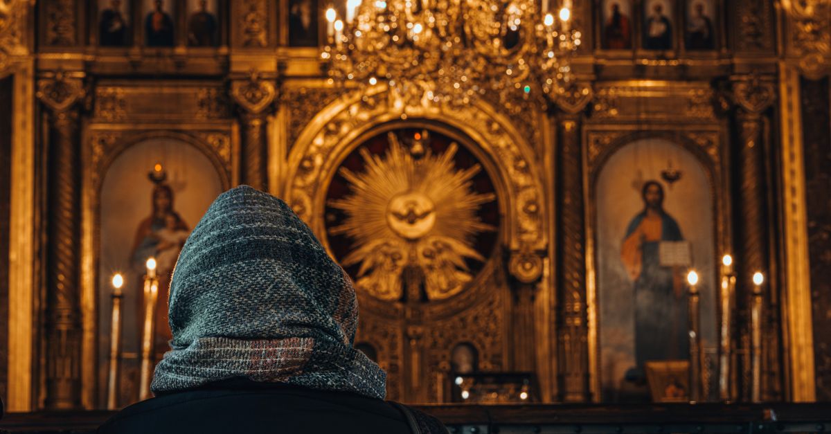 A person in a headscarf sits before an ornate church altar in İstanbul, Türkiye, with chandeliers above.