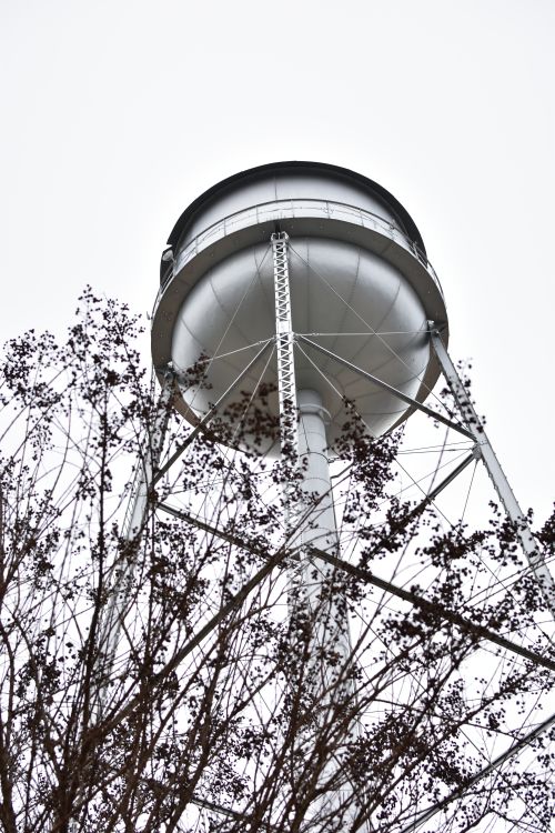 Free Low-angle view of a metal water tower framed by bare branches on an overcast winter day. Stock Photo