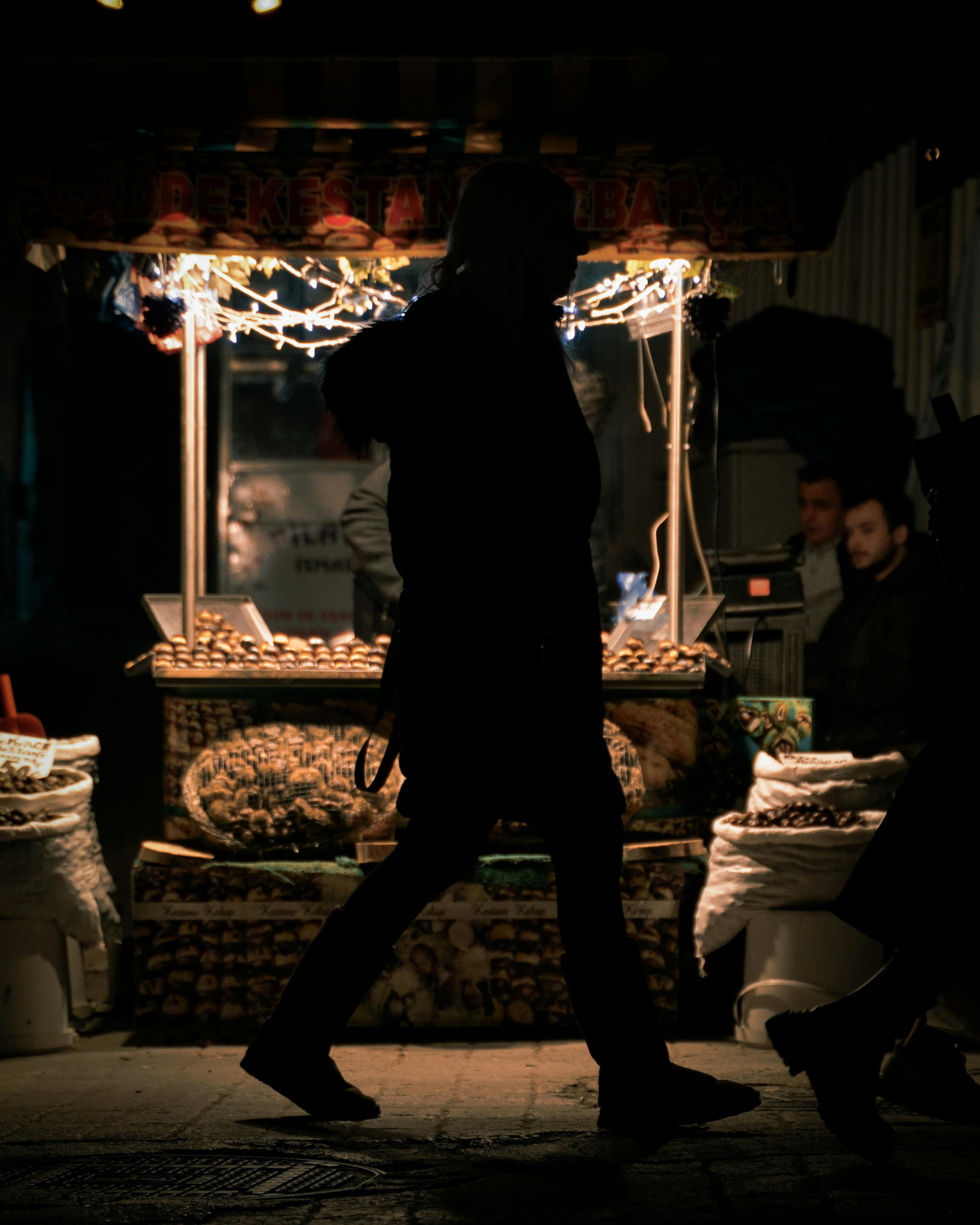 Gratis Silhuett av en person foran en livlig nattmarkedsbod utsmykket med lys. Arkivbilde