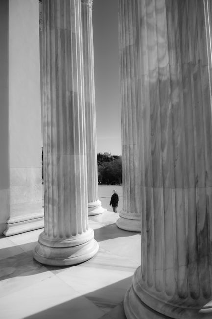 Dramatic black and white photo of ancient columns with a solitary figure, evoking a sense of history.