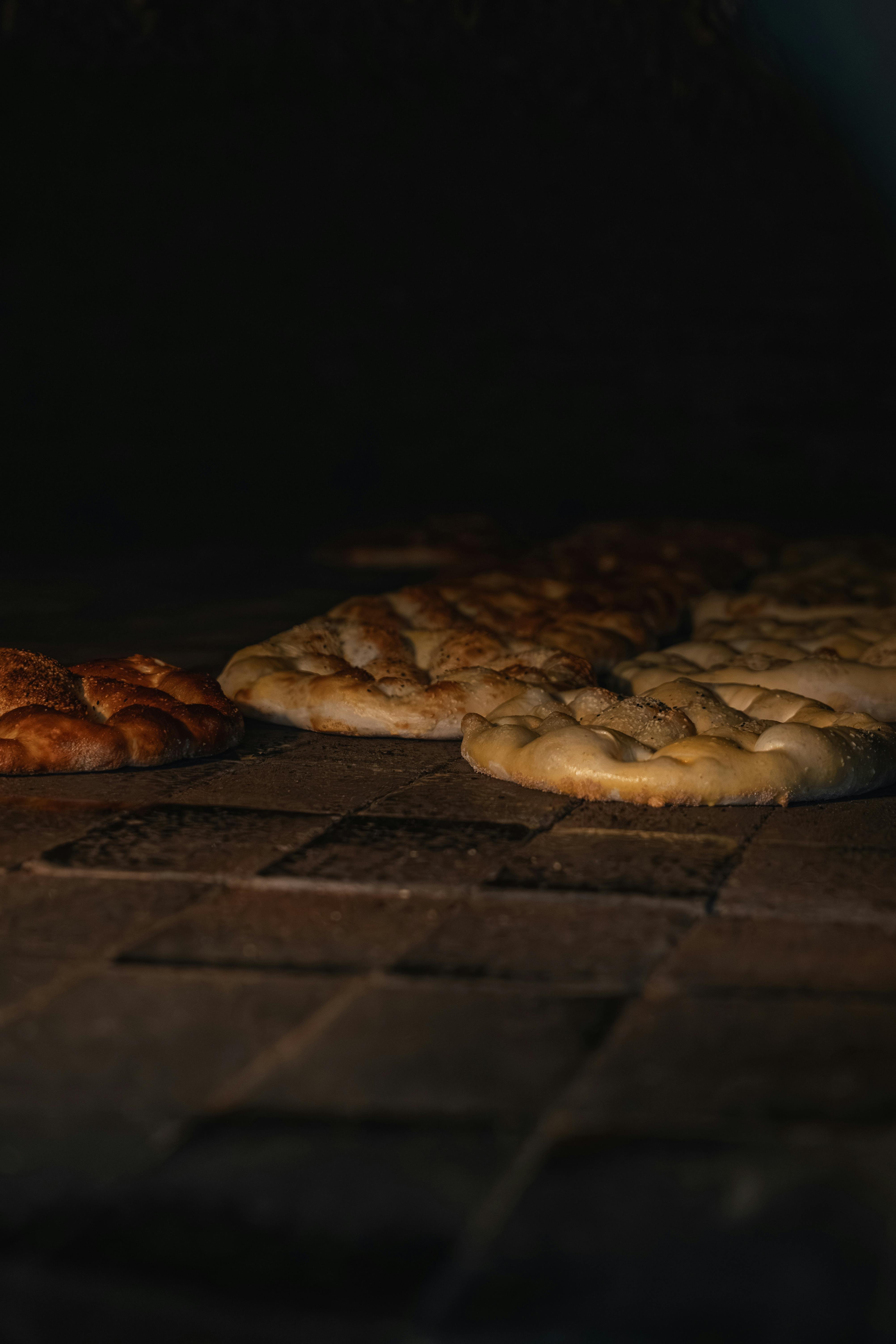 Gratis Una calda illuminazione mette in risalto il pane piatto appena sfornato, disposto su una rustica superficie in pietra. Foto a disposizione