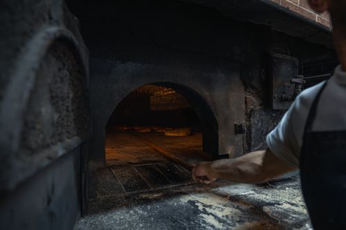 Free Baker using traditional oven for fresh bread preparation in a rustic setting. Stock Photo