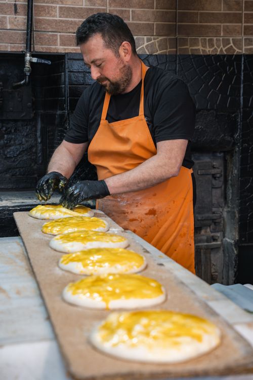 Free Baker in orange apron preparing cheese breads in a rustic kitchen setting. Stock Photo