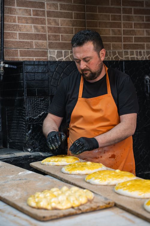 Free A baker in an orange apron skillfully prepares traditional bread in a rustic kitchen setting. Stock Photo