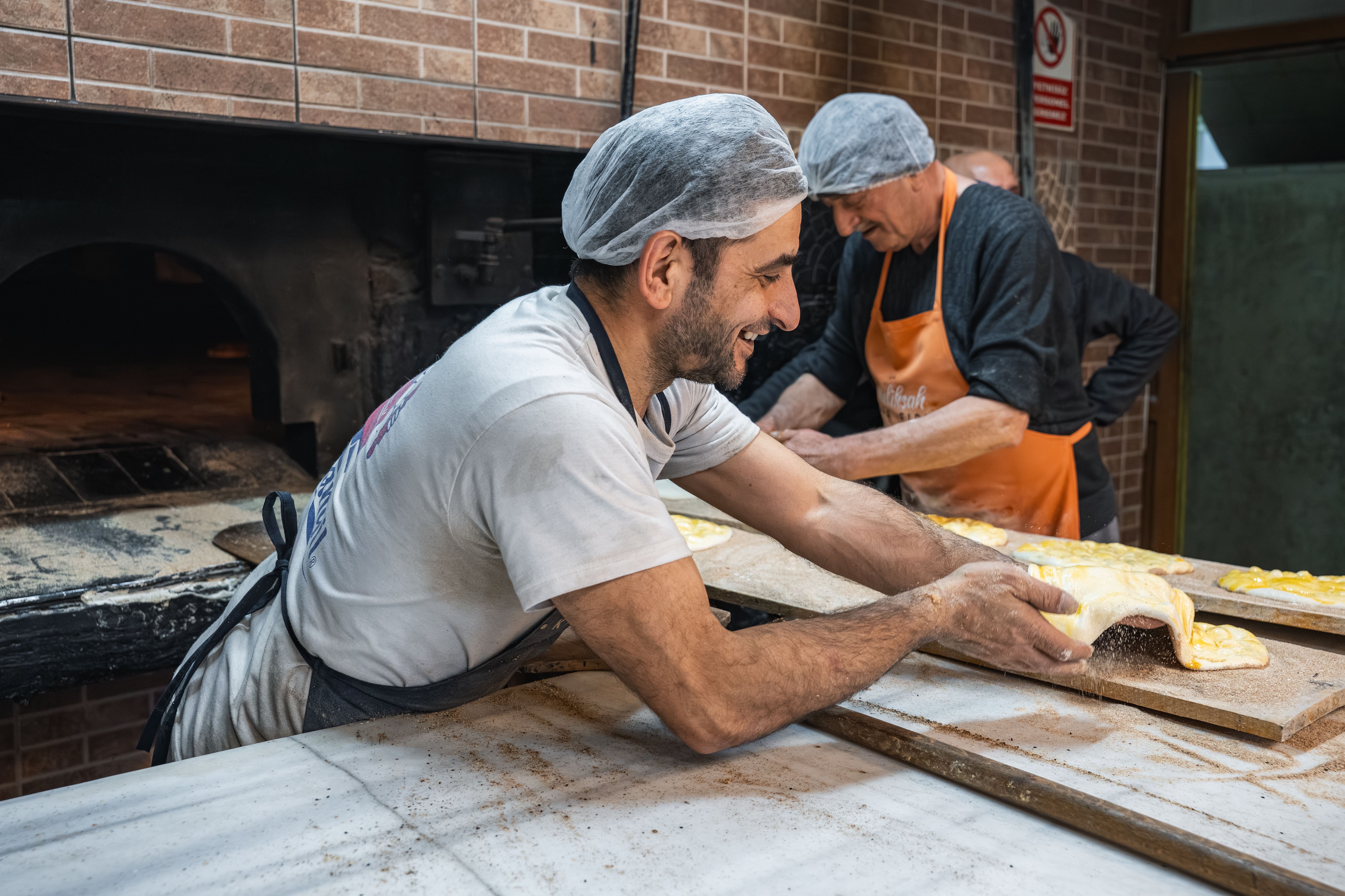 Two bakers working together to prepare bread in a traditional oven setting.