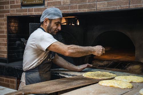 Free Baker sprinkles spice on bread before baking in a stone oven. Stock Photo