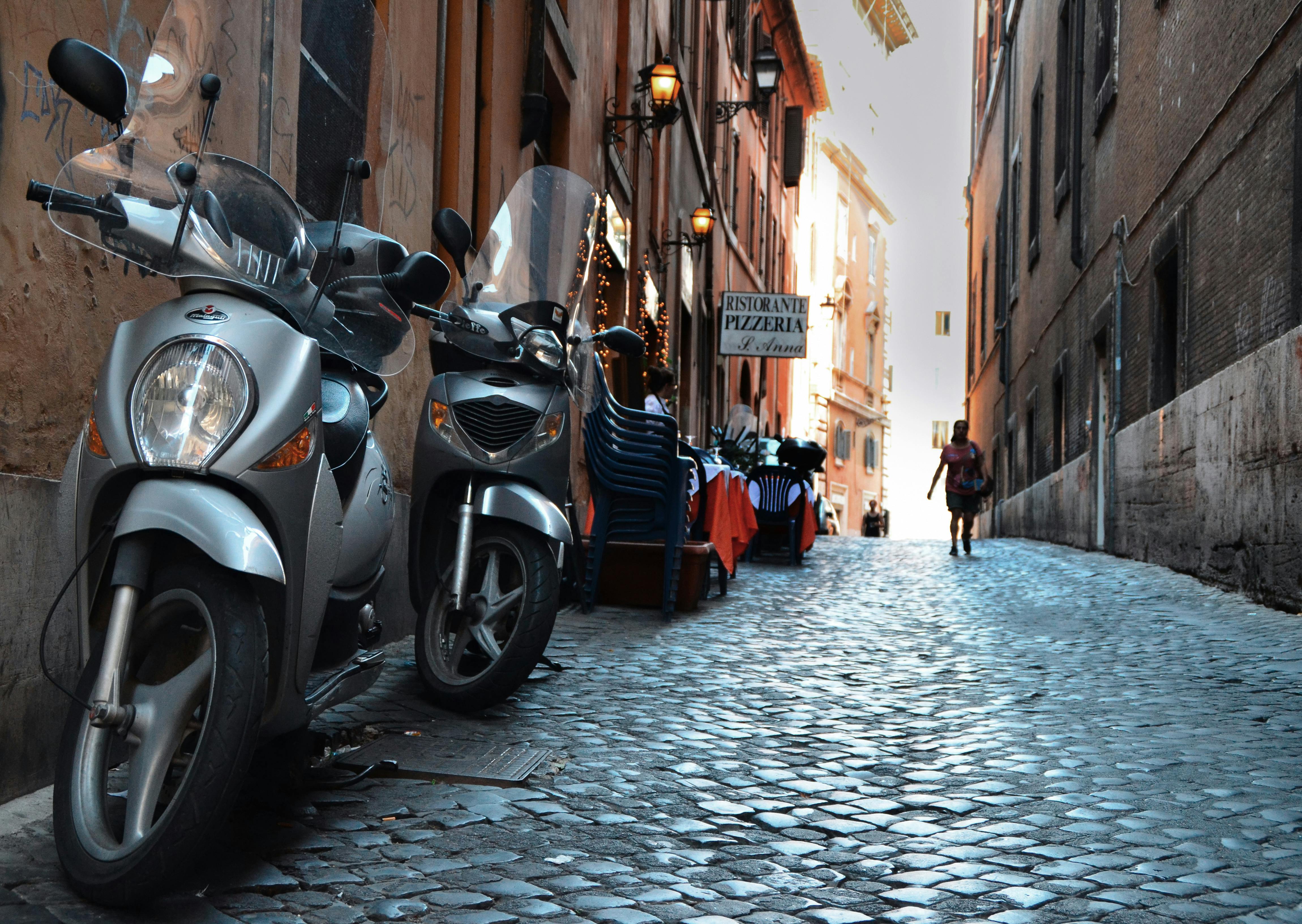 Cobblestone street in Rome with parked scooters and a quaint pizzeria along the alley.