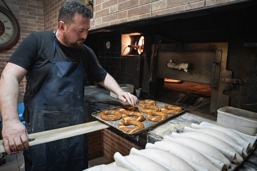 A skilled baker places a tray of freshly baked pretzels into a traditional brick oven.