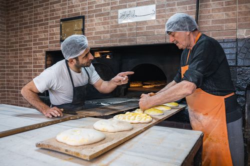Free Two bakers preparing traditional bread in a rustic oven setting, showcasing cultural baking techniques. Stock Photo
