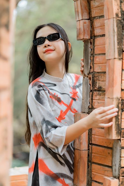 Free Stylish woman wearing sunglasses and a colorful shirt poses by a brick wall outdoors. Stock Photo