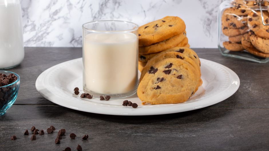 A stack of thick, golden-brown chocolate chip cookies studded with melted milk chocolate chips, one broken in half showing a soft, gooey center.