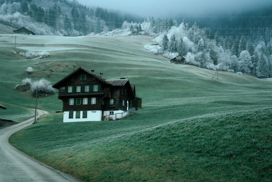 Scenic winter view of a traditional Swiss chalet surrounded by frosted alpine hills and forests in Switzerland.