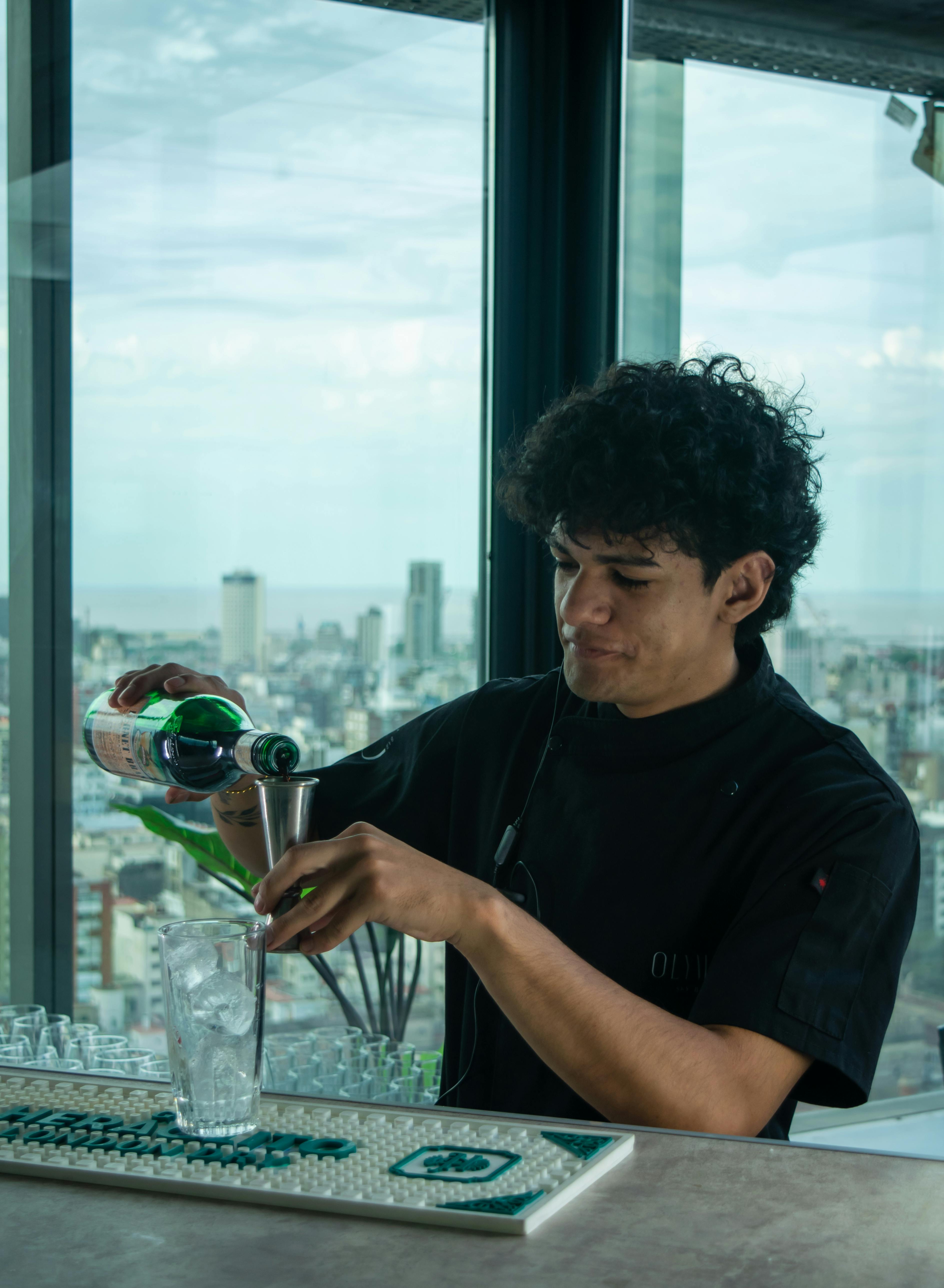 Bartender skillfully mixing a cocktail with city skyline view from rooftop bar.