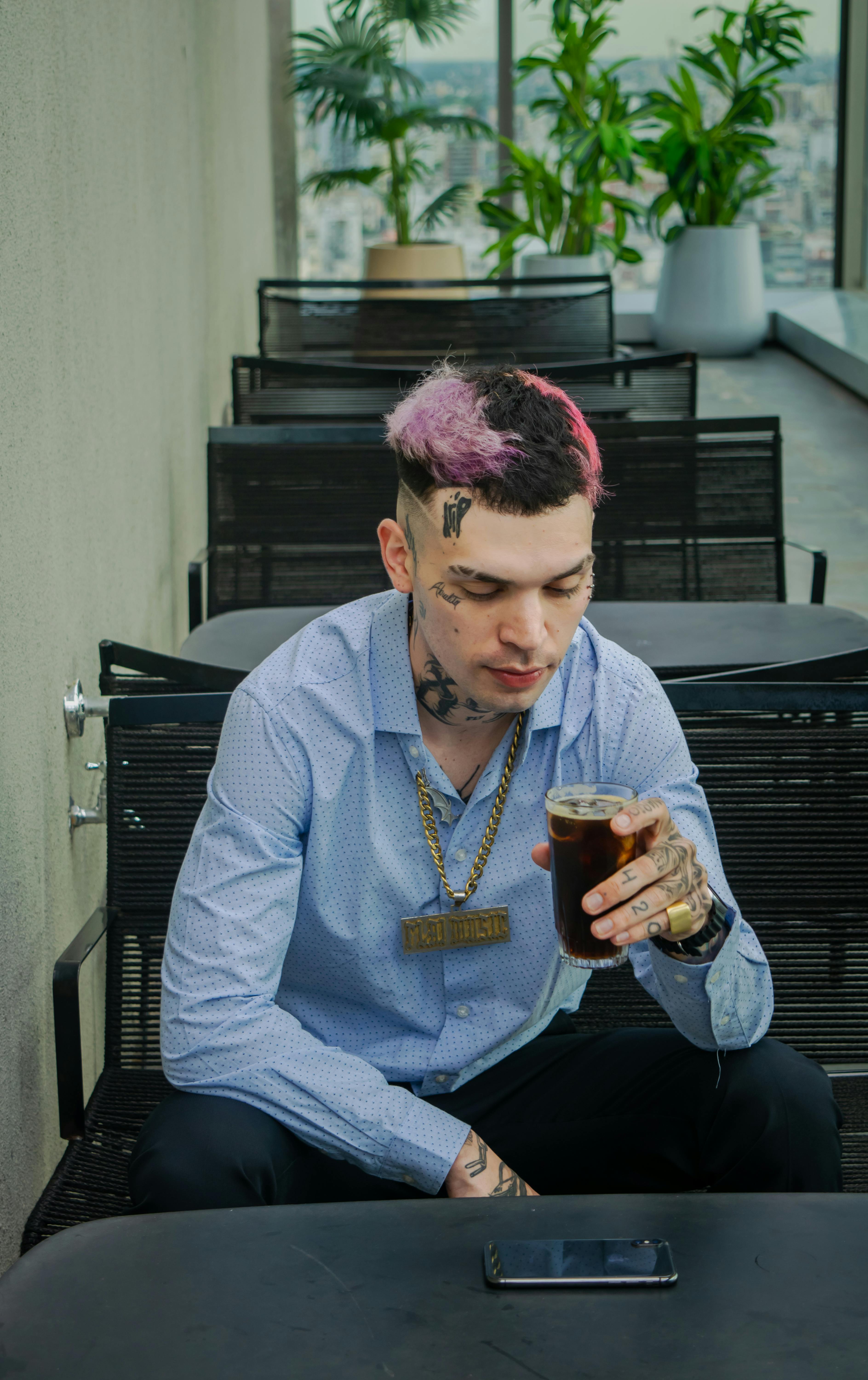 Young man with tattoos and dyed hair enjoying a coffee at an indoor cafe.