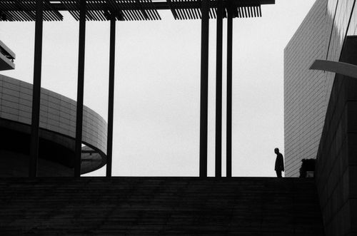 Free Black and white silhouette of a person amidst modern architectural structures, creating a striking contrast. Stock Photo