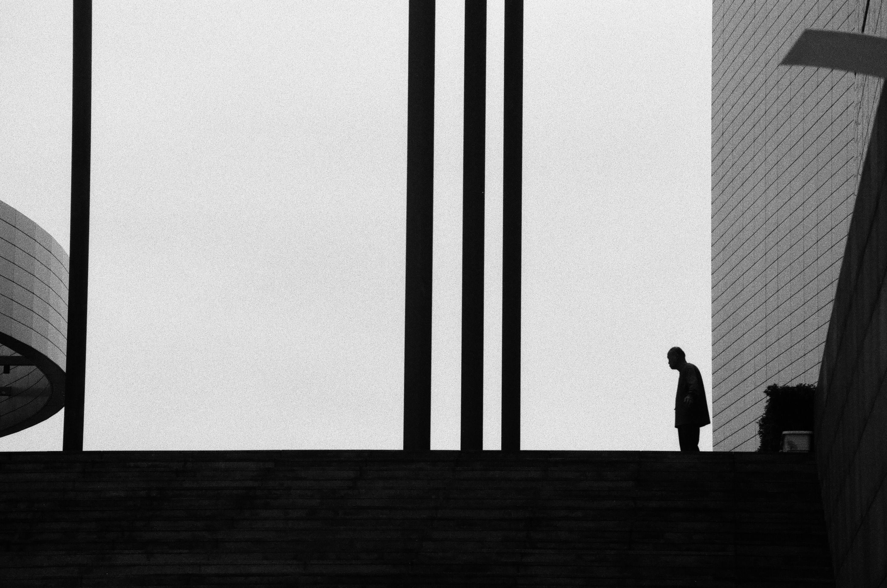 Kostenlos Düstere Schwarz-Weiß-Aufnahme eines einsamen Mannes in einer kargen architektonischen Umgebung. Stock-Foto