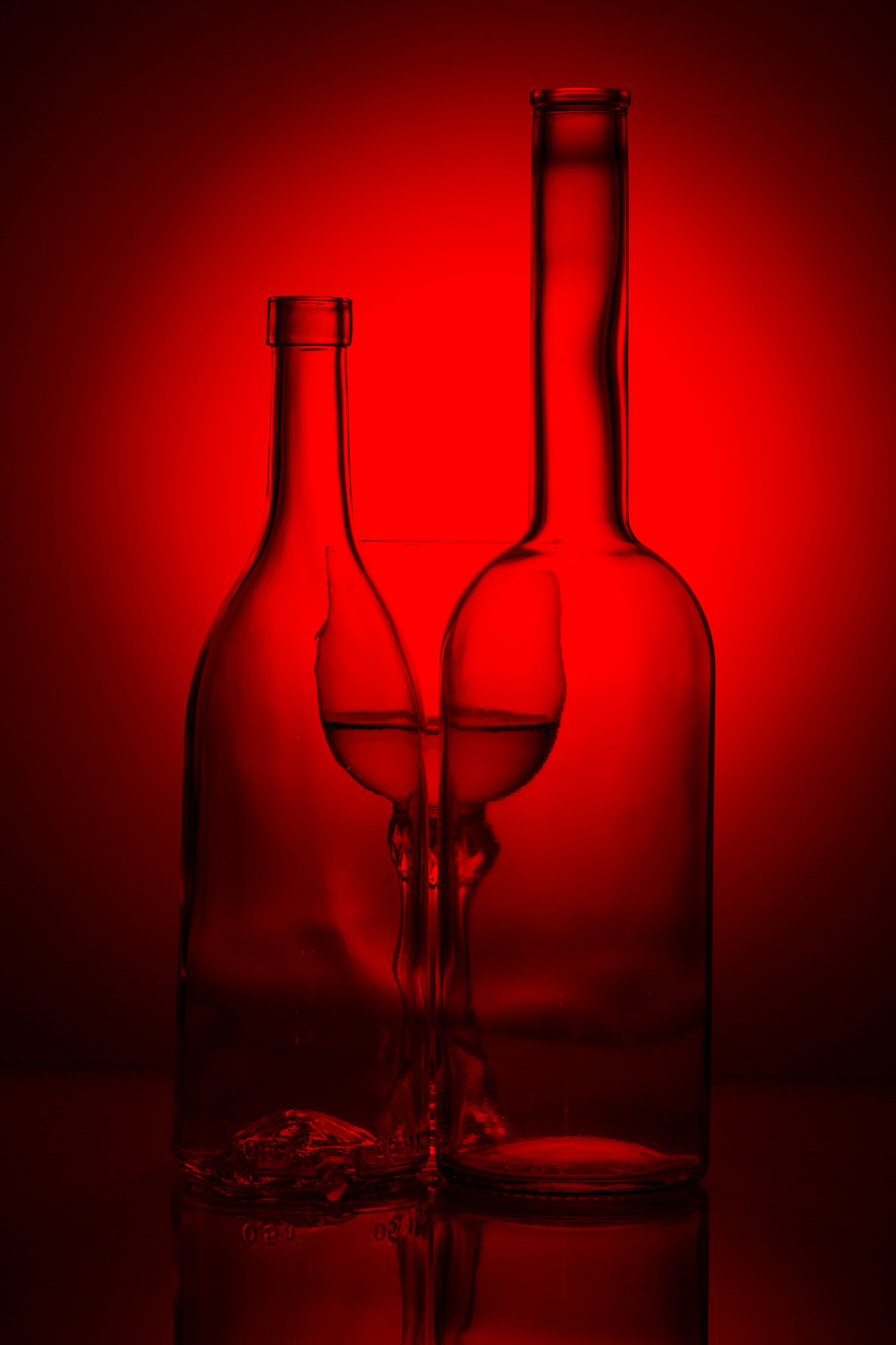 Stunning silhouette of glass bottles and wine glass against a vivid red backdrop, creating an artistic composition.