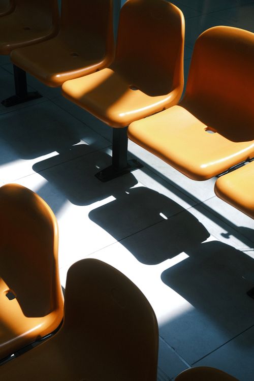 Free A row of orange plastic chairs with dramatic shadows in a bright indoor setting. Stock Photo