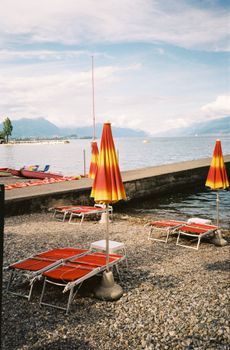 Vibrant lakeside view with orange umbrellas and lounge chairs on a sunny day.