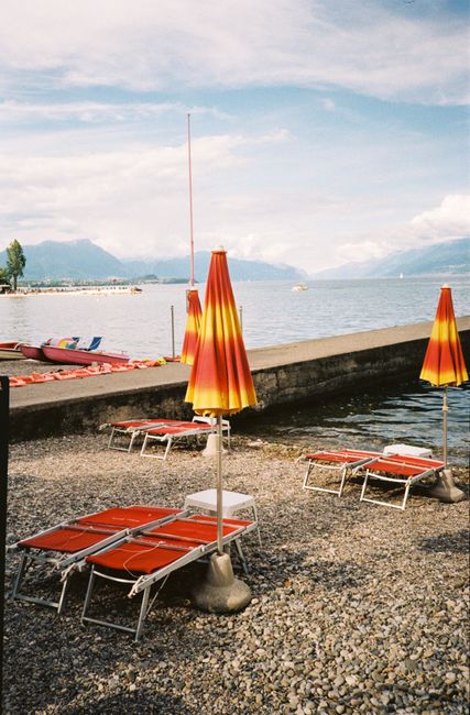 Vibrant lakeside view with orange umbrellas and lounge chairs on a sunny day.