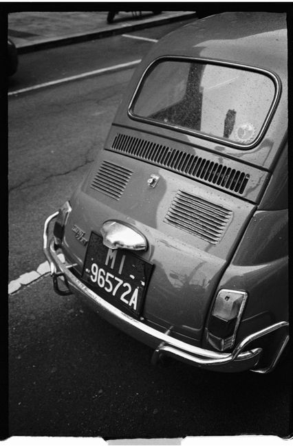 Classic Fiat car parked on urban street in black and white, evoking nostalgic charm.