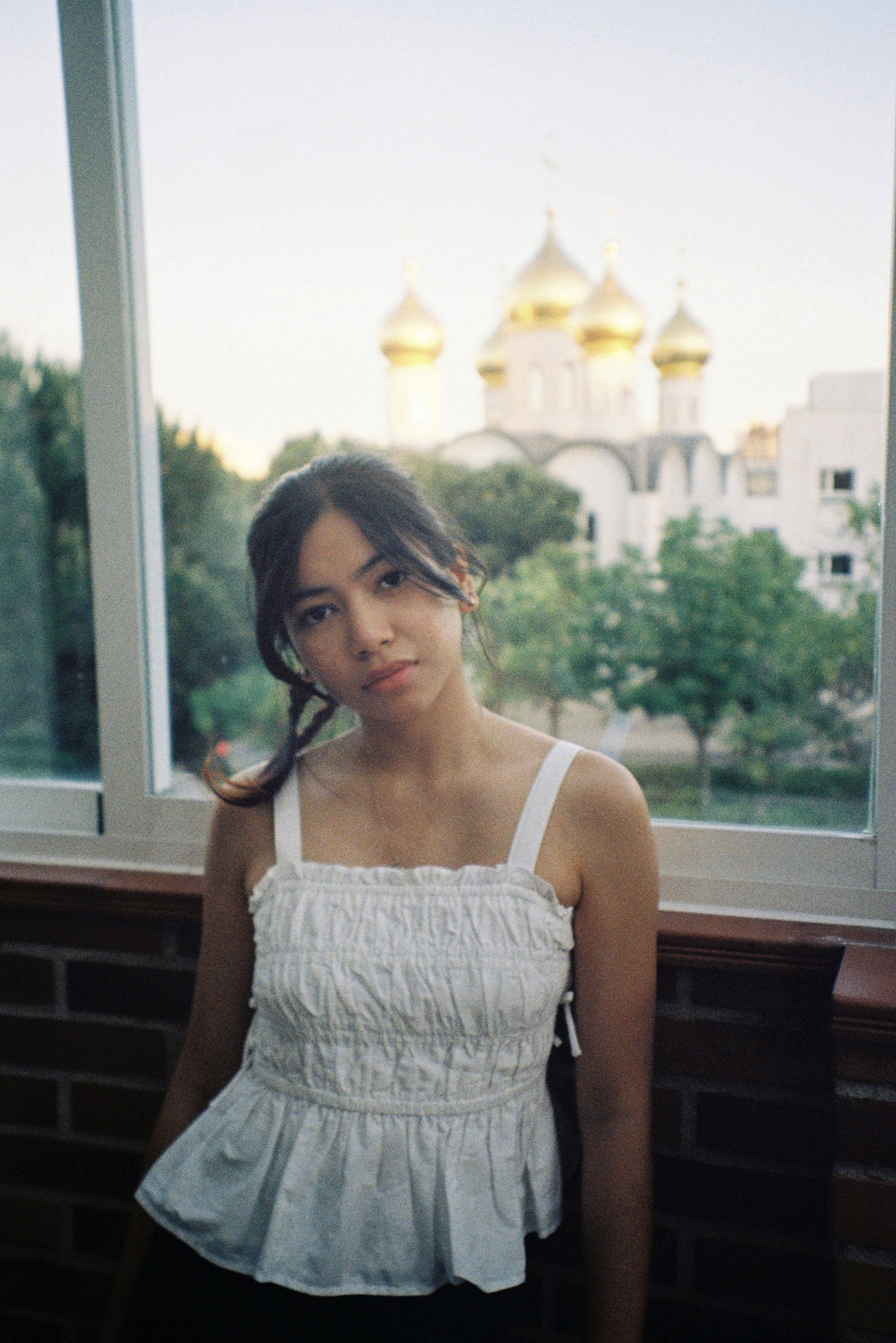 Portrait of a young woman indoors with Spanish Orthodox church in Madrid visible outside.