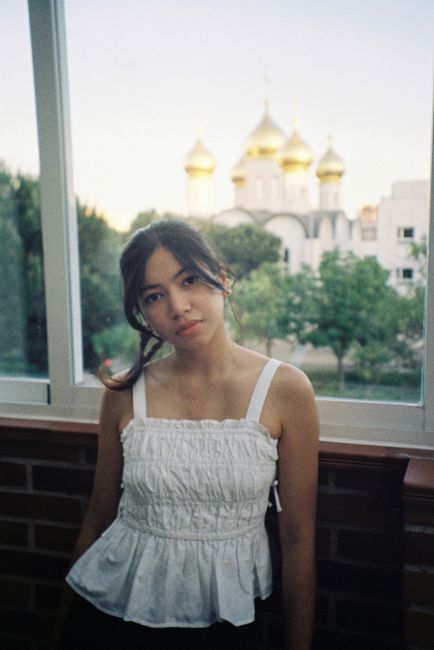 Portrait of a young woman indoors with Spanish Orthodox church in Madrid visible outside.
