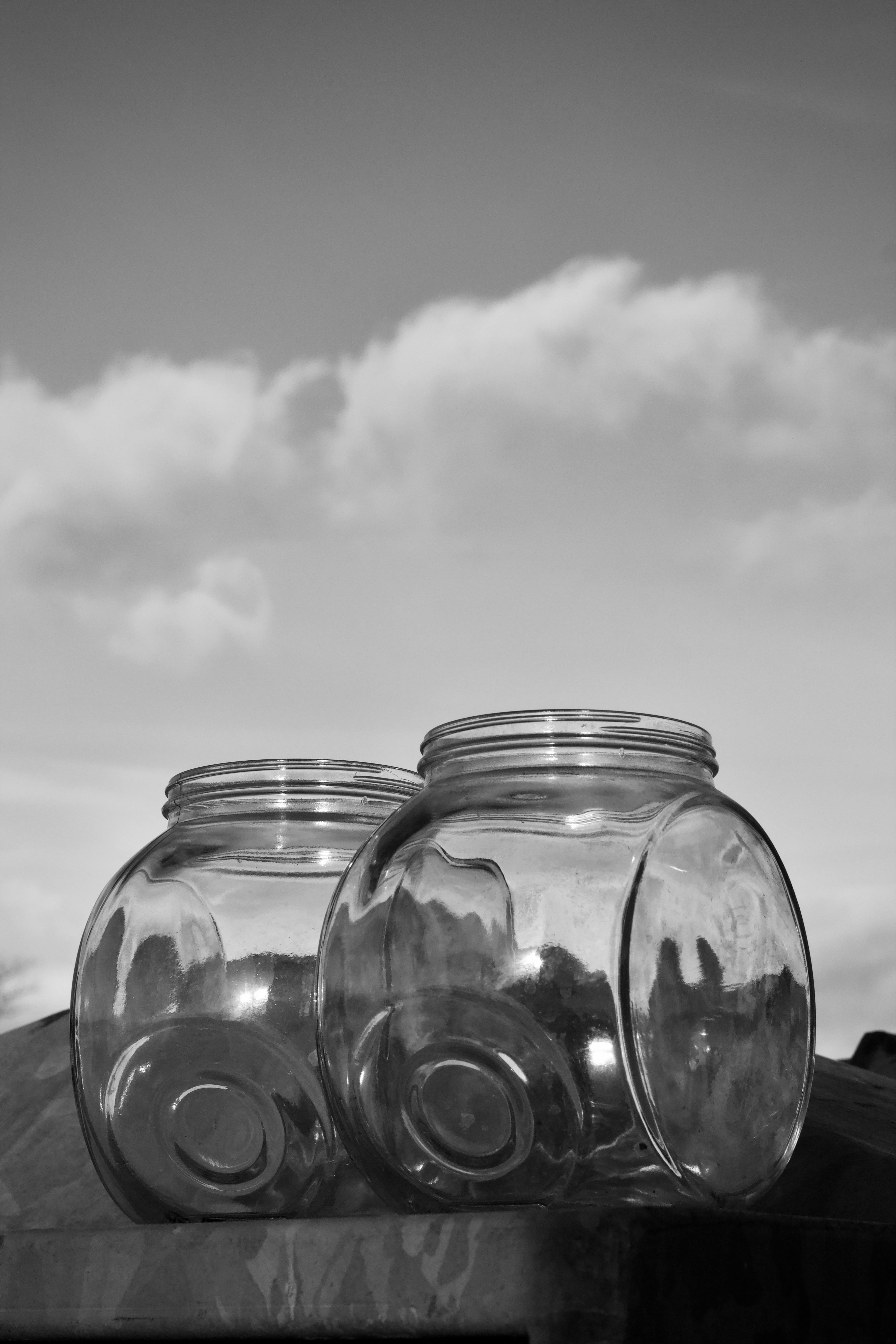 無料 曇り空を背景にした 2 つの空のガラス瓶の芸術的な白黒写真。コントラストと質感が強調されています。 写真素材