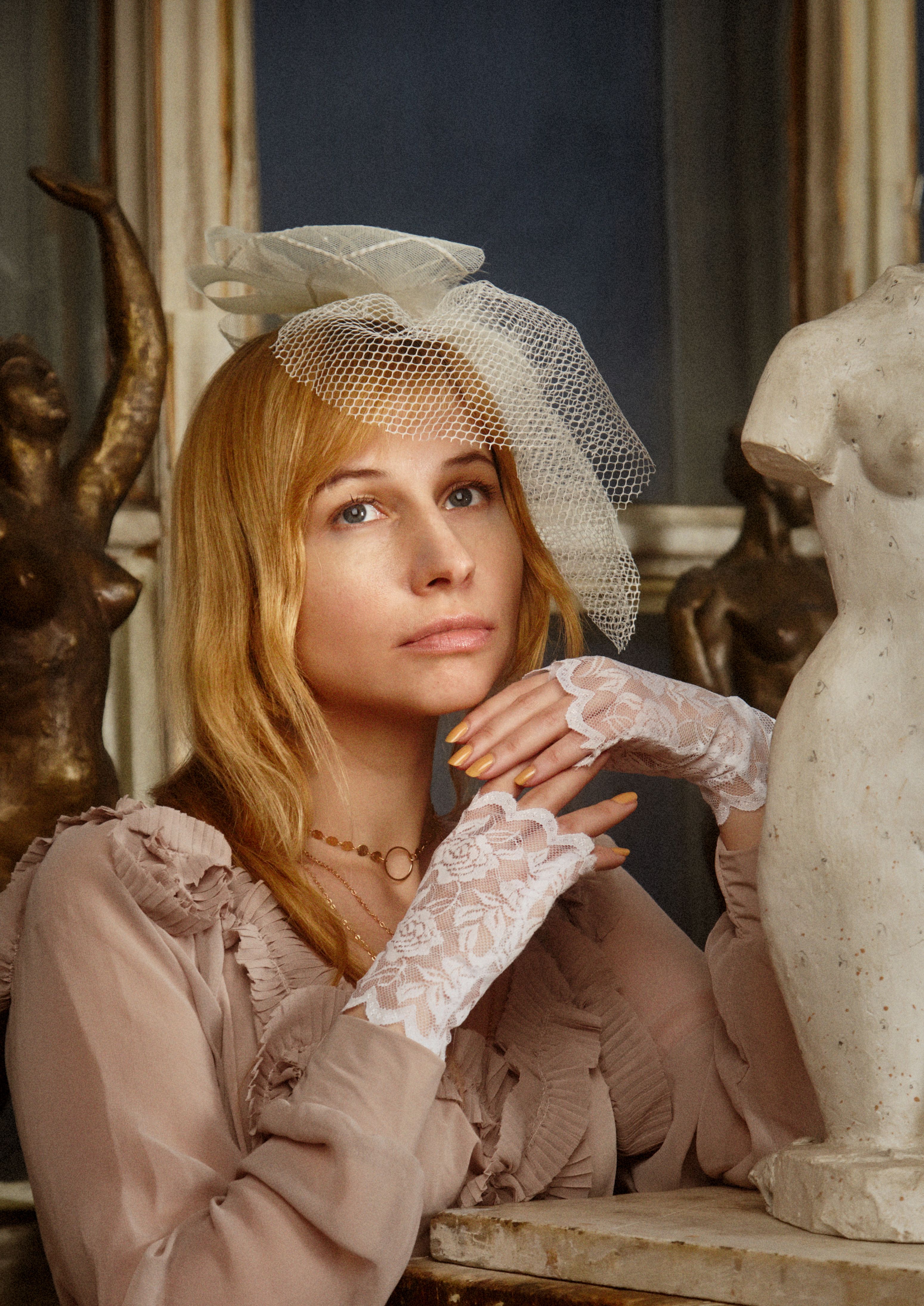 A portrait of a woman in vintage clothing and veil, surrounded by sculptures, exuding elegance and grace.