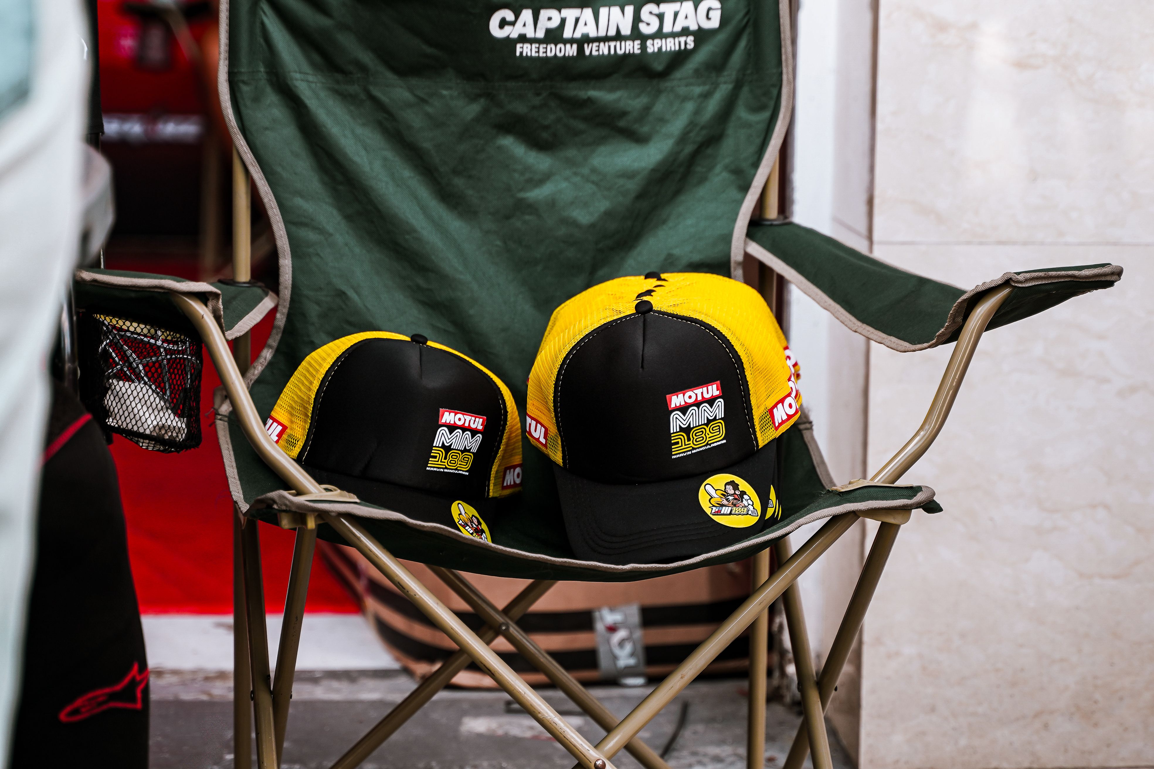 Black and yellow caps with Motul branding on a green foldable chair indoors.