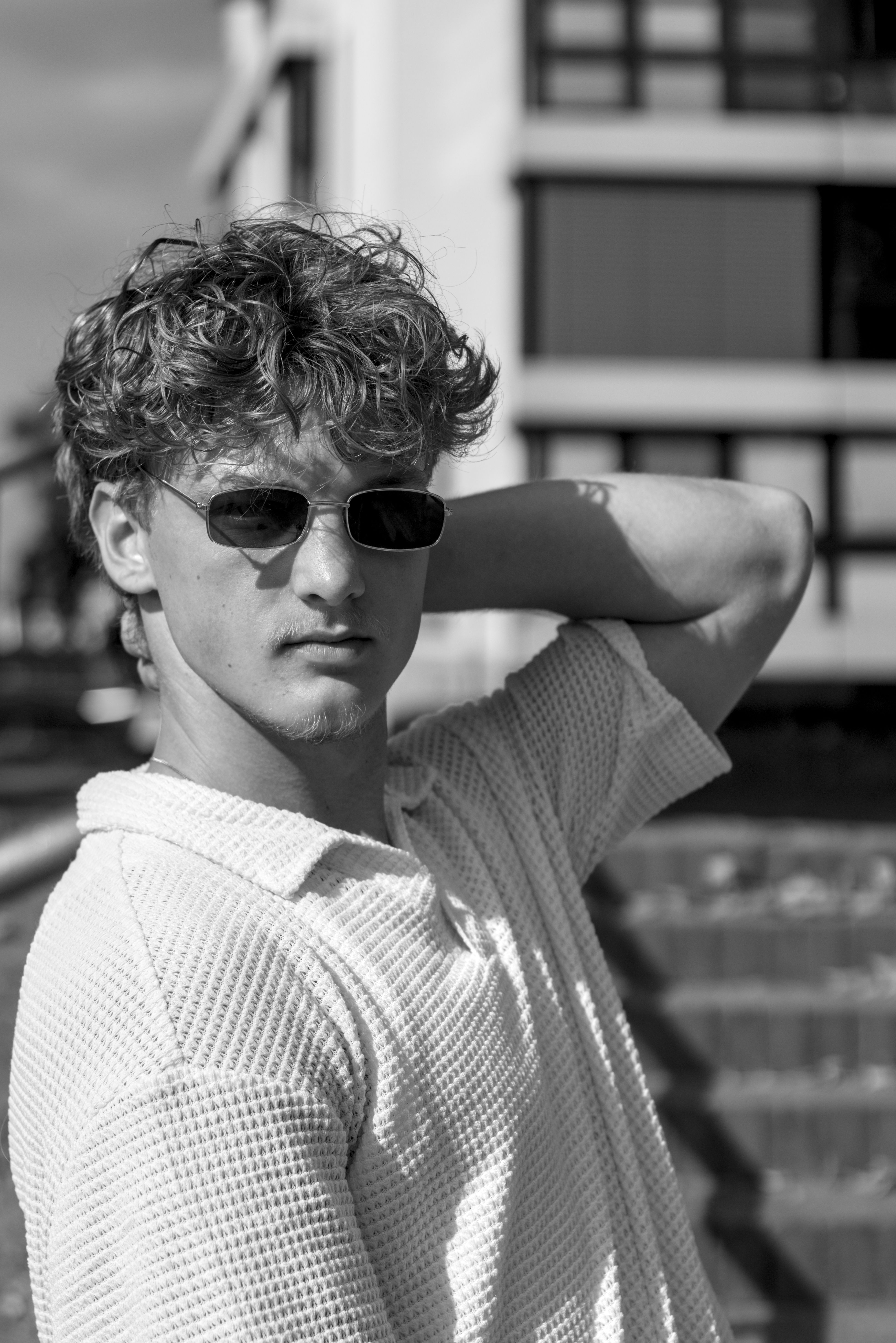 Black and white portrait of a stylish young man in sunglasses, showcasing modern fashion in an urban setting.
