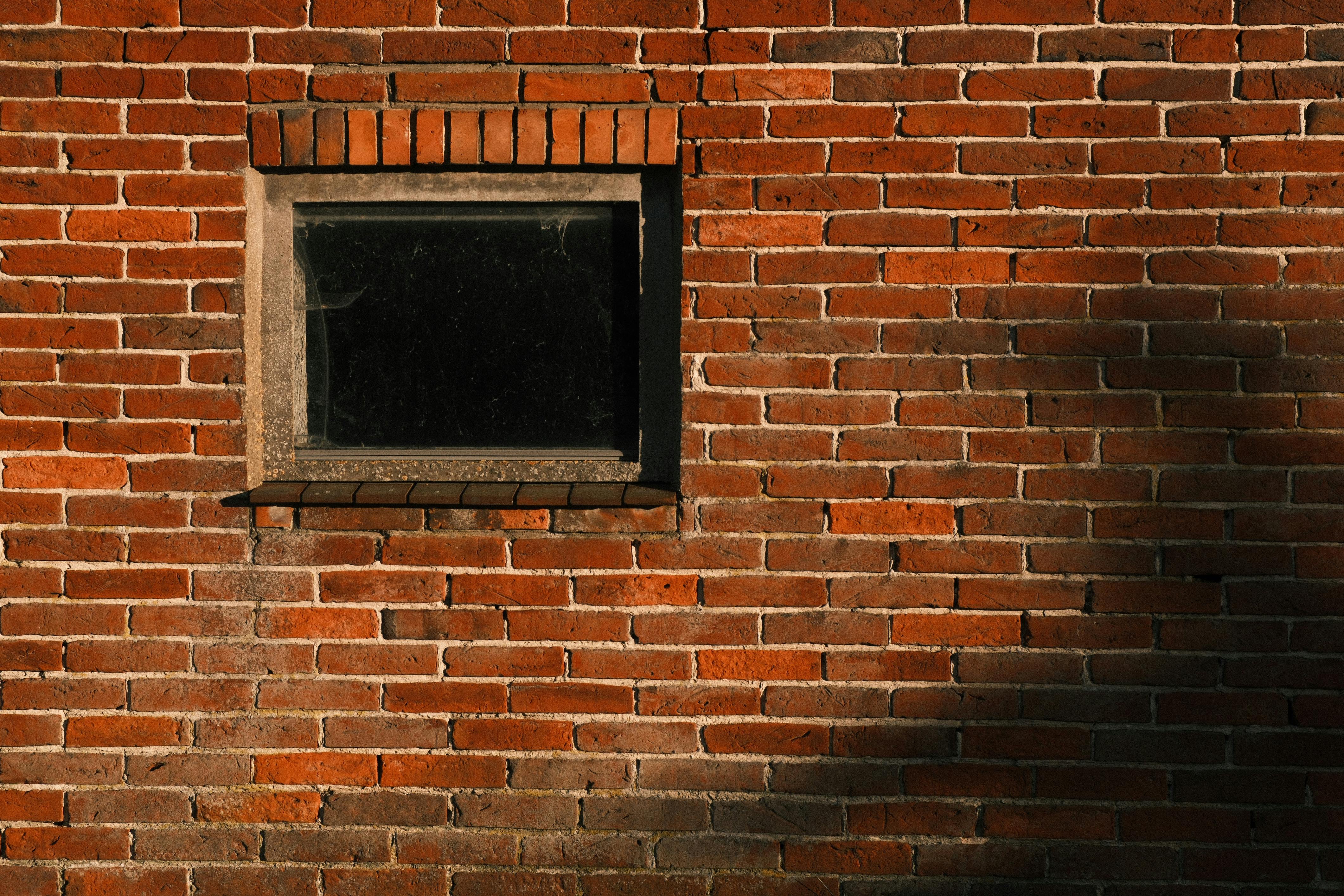Gratis Primer plano de una pared de ladrillos rojos con una ventana vintage que proyecta sombras. Foto de stock