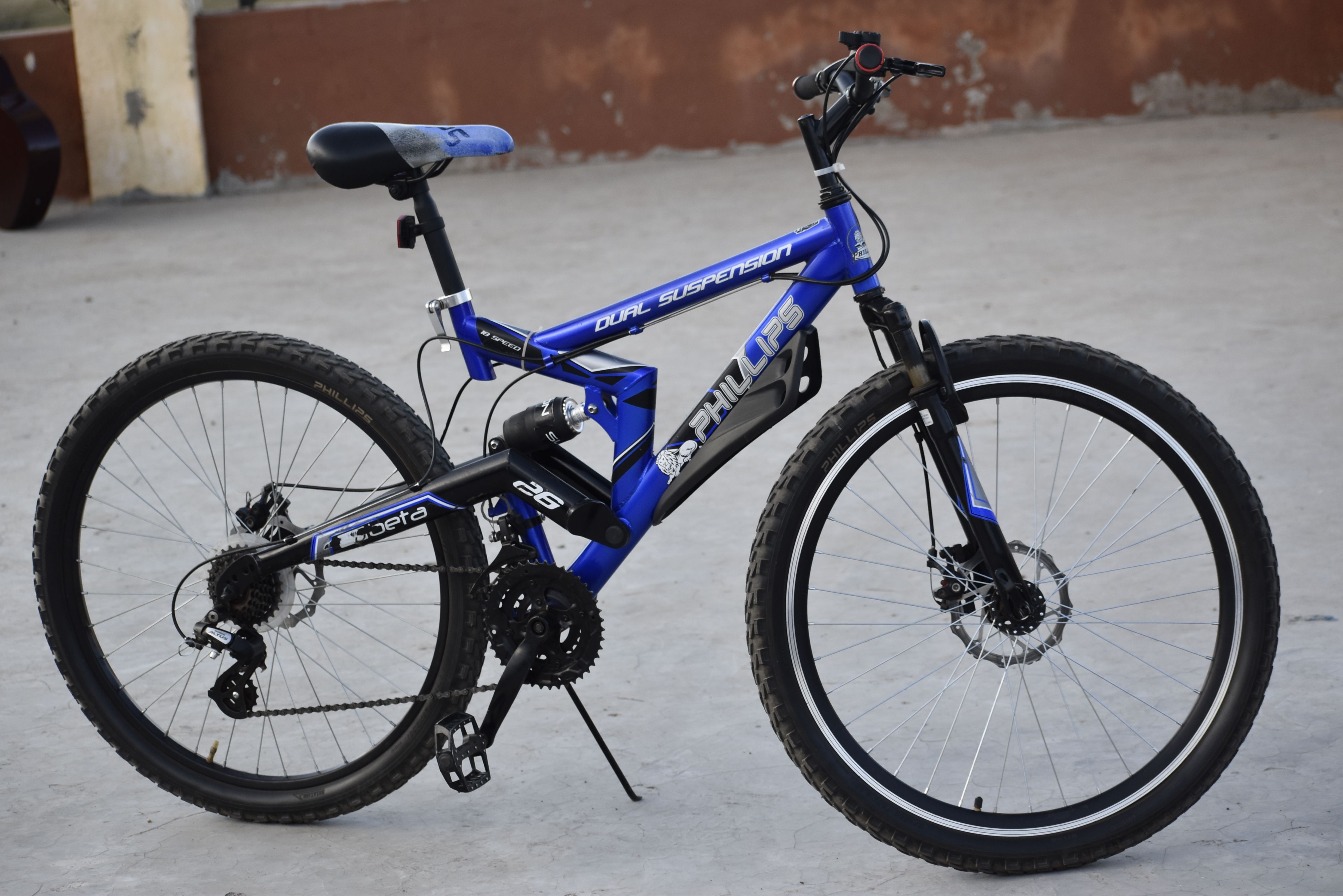 Blue mountain bike with dual suspension photographed outdoors on a concrete surface.