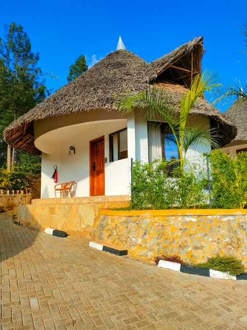 Free Idyllic cottage with thatched roof under clear blue sky, surrounded by greenery. Stock Photo