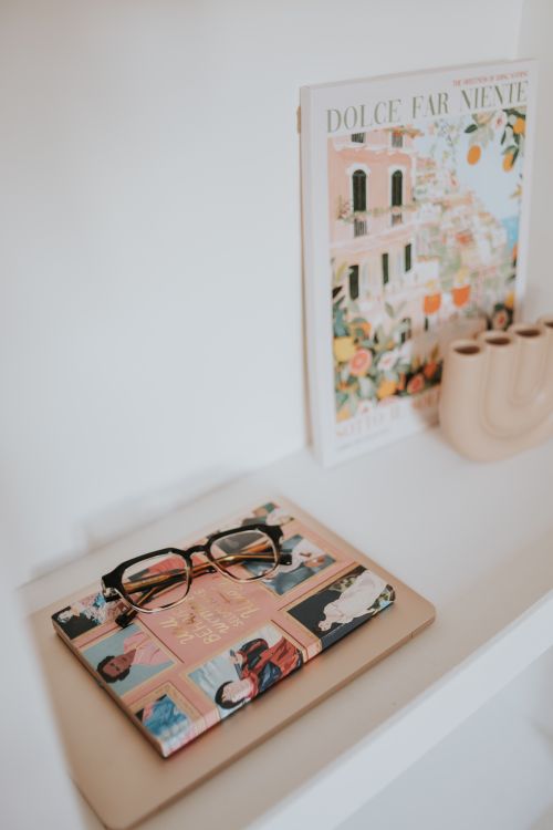 Free Elegant workspace featuring glasses, notebook, and Italian-themed art for a cozy atmosphere. Stock Photo