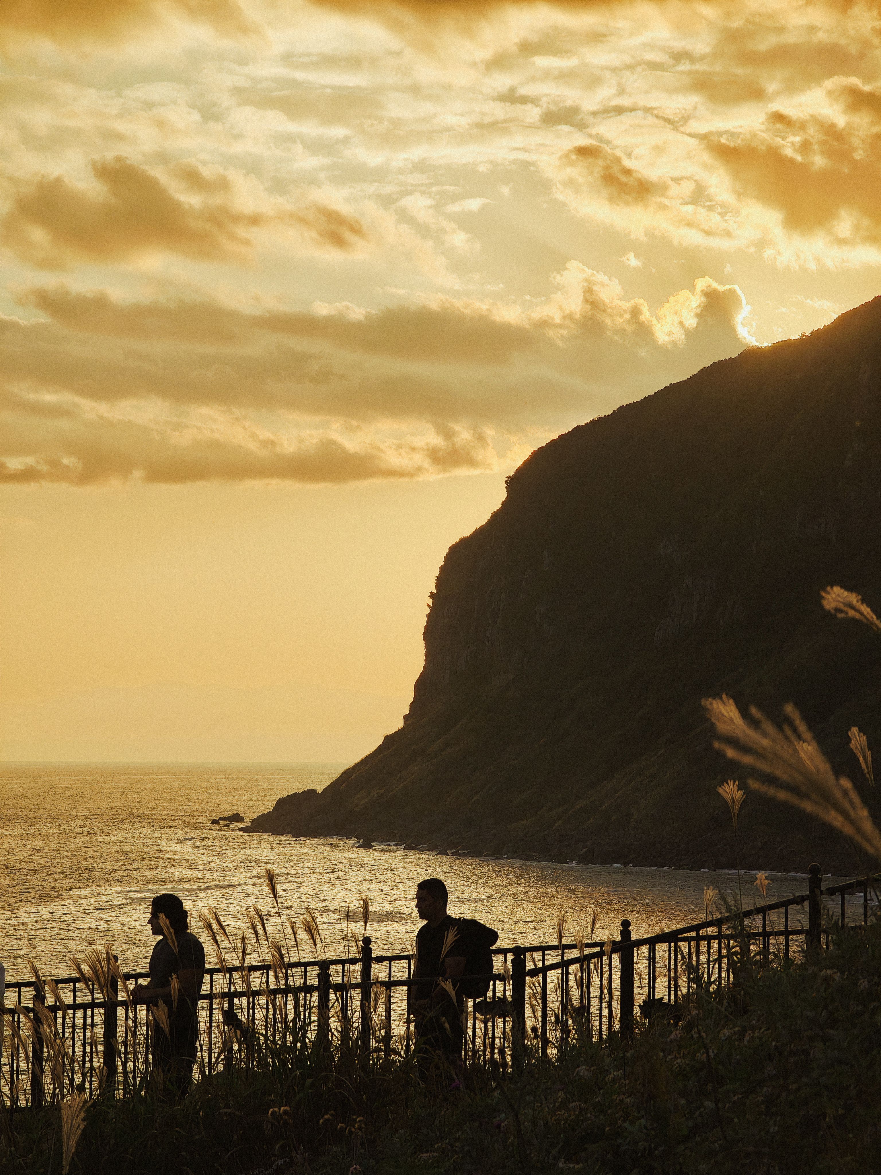 Silhouetted figures stroll along the coast in Hakodate at sunset, Hokkaido, Japan.