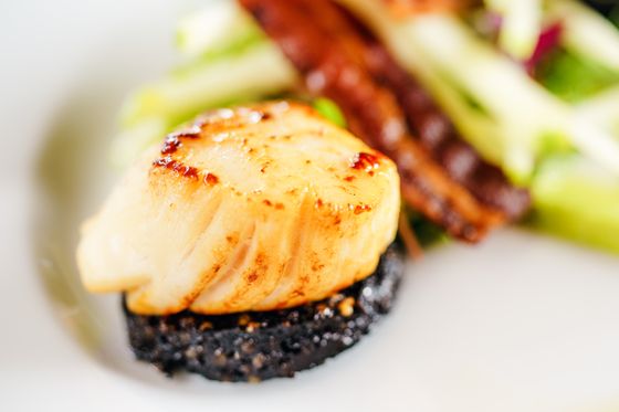 Close-up of a golden seared scallop on a black pudding round with bacon and apple matchsticks