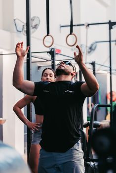 Athletic man and woman exercising with gymnastic rings indoors in a modern gym setting.